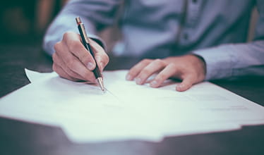 A person writing on a sheet of paper with a pen.